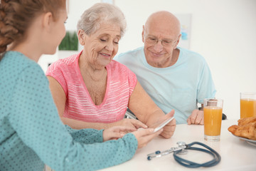 Young caregiver teaching senior couple to handle with tablet computer at home