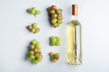 Obraz premium Bottle with white wine and fresh ripe juicy grapes on light background, top view