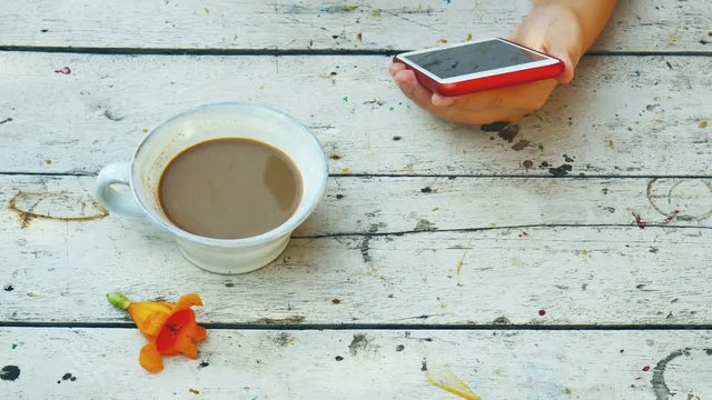 Woman husing smartphone with cup of coffee and yellow flower on wooden desk.
