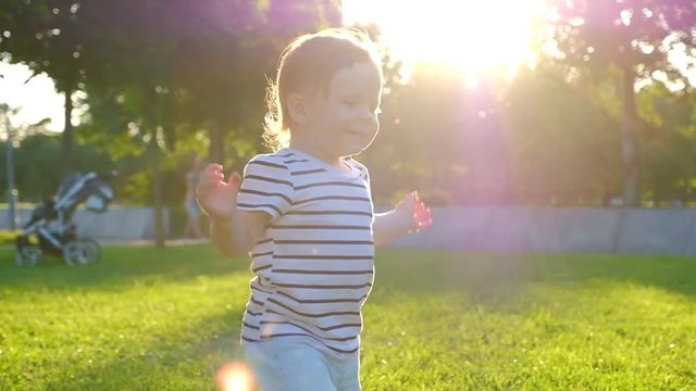 Cute Little baby girl walks by grass at sunset in a park in suumer day. Slow Motion. Happy childhood. Family