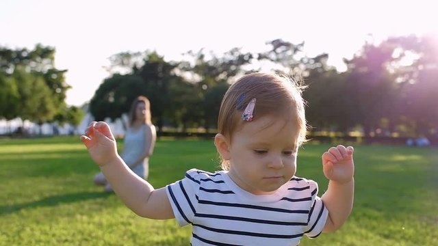 Cute Little baby girl walks by grass at sunset in a park in suumer day. Slow Motion. Happy childhood. Family