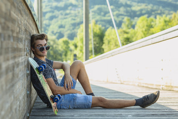 Boy sitting near skateboard at bridge