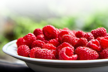 Fresh ripe raspberries in a white bowl on blurred background