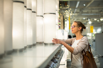Pretty, young woman choosing the right light for her appartment in a modern home furnishings store (color toned image; shallow DOF)
