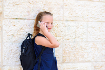 Outdoor portrait of happy girl 8-9 year old talking on phone. Cute schoolgirl with backpack talking on cell phone and smiling.