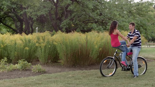 HD A yound couple is sitting on one bycile looking at each other and cahtting