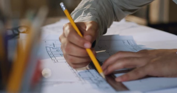 Male Caucasian hands drawing on the plan with a pencil and rule on the table. Close up of the architect working.