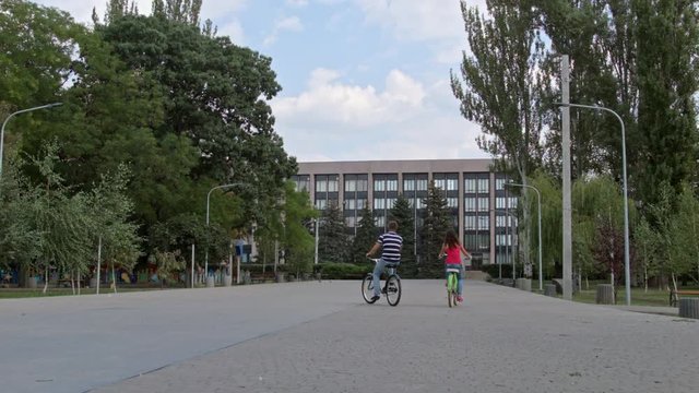 HD A Couple riding bicycles in the park, on block stones view from back