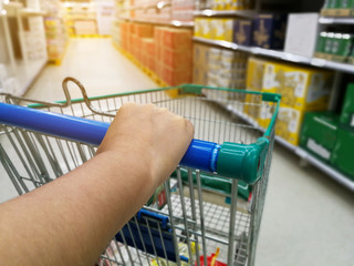 Asian woman shopping in supermarket store and checking her smartphone with pushing shopping cart,blur background
