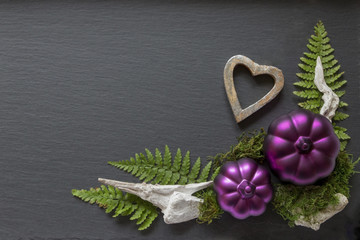 silbernes Herz mit Ornament aus 2 lila Kürbissen  und Farn  unten rechts auf Hintergrund aus Schiefer