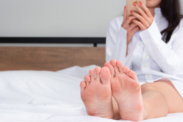 Teenagers phone on a bed,  toes showing under the sheet.
