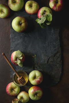 Ripe organic gardening green red apples with leaves and jar of honey on black slate board over dark texture background. Flat lay, space. Autumn harvest.