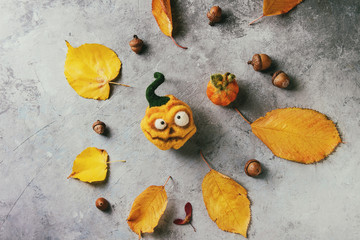 Funny craft Halloween needle felted pumpkins jack o lantern holiday decor with autumn yellow leaves and acorns over grey texture background. Flat lay, copy space