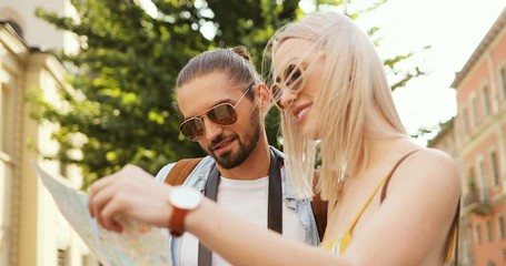 Close up of the couple of young attractive tourists reading a map while being in a new town on a summer day.