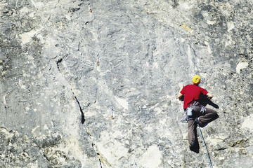 Young man looking up while climbing challenging route on cliff.