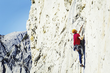 Young man looking up while climbing challenging route on cliff.