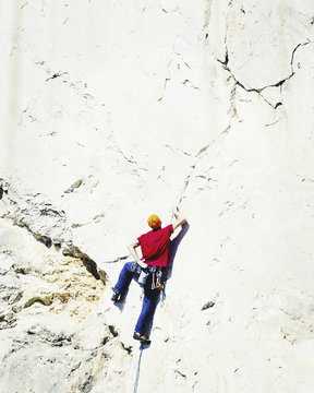 Young man looking up while climbing challenging route on cliff.