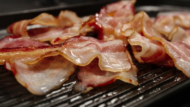 CLOSE UP: Heap of fried strips of bacon on a pan