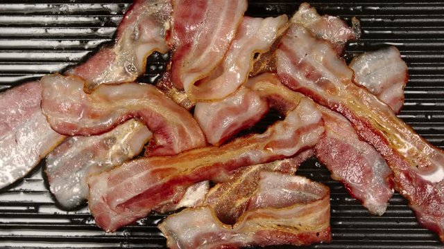 TOP VIEW: Heap of strips of bacon are frying on a black pan