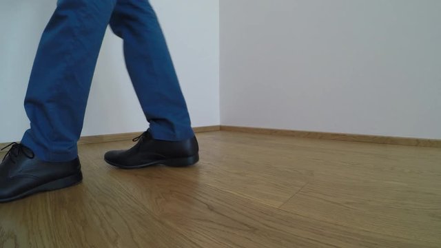 Man wearing blue shoes and trousers, washes the parquet floor with the yellow mop