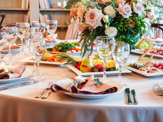 Table served for wedding banquet with cutlery and flowers in vases. Salads, appetizers and glasses with wine.