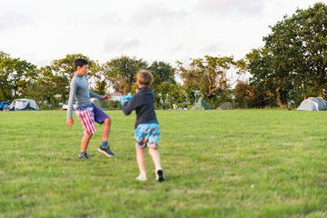 two brother boys not in focus playing with ball and having fun together over camping field in England