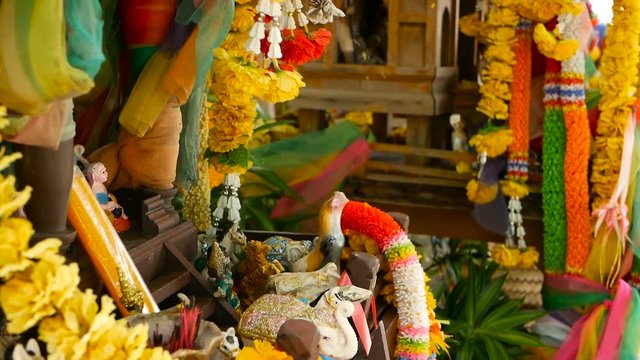 Wooden miniature guardian spirit house. Small buddhist temple shrine, colorful flower garlands. San phra phum erected to bring fortune. Traditional respect animistic rituals, pray ceremonies