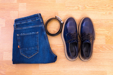 Men's jeans, leather belt and a pair of blue glossy shoes on wooden floor