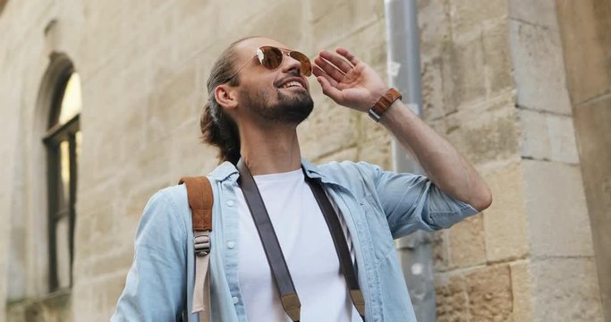 Caucasian young attractive man walking and doing sightseeing with camera as being a tourist in the old city.
