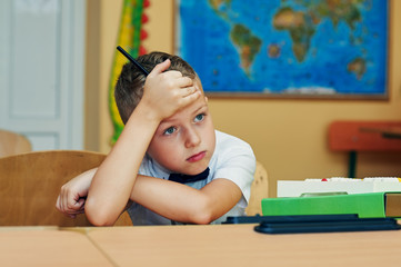 Tired elementary school kid in class .Pensive and tired boy in elementary school class