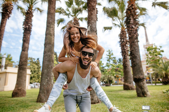Playful sportive bearded man giving piggyback ride to woman on beach. Young people having fun on the beach and piggybacking.