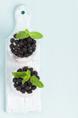 Fresh healthy dessert with blackberries at top on wooden board on pastel blue background with copy space.
