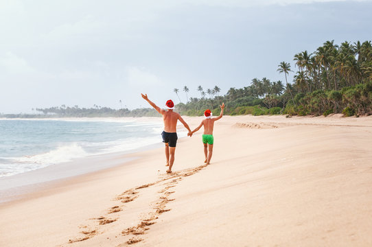 Father and son in Santa's hats run on perfect sand beach on tropical island. Christamas and New Year holiday vacation