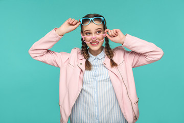 Happy funny girl in casual or hipster style, pigtail hairstyle, standing, holding two blue and pink...