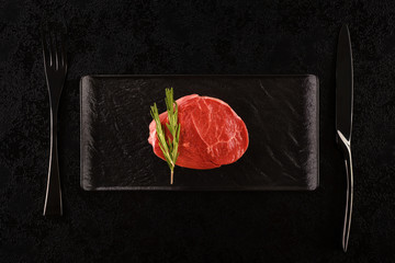 Raw steak on black plate.