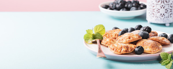 Dutch mini pancakes called poffertjes with blueberries, sprinkled with powdered sugar. Healthy food concept with copy space. Banner. © Iryna Melnyk