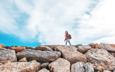 Obraz premium Beautiful young woman traveler walking on rocks rocks against the blue sky in hat and sunglasses Algarve, Portugal
