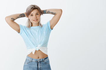 Ready for summer. Athletic attractive european girlfriend with blonde hair in cropped top, holding hands behind head and smiling broadly, showing new tattoos on arms and hanging out with friends