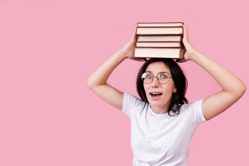 Beautiful student holding a stack of books on her head on a pink background