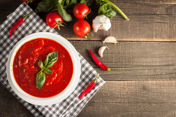 Fresh, healthy tomato soup with basil, pepper, garlic, tomatoes and bread on wooden background. Spanish gazpacho soup.