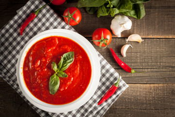 Fresh, healthy tomato soup with basil, pepper, garlic, tomatoes and bread on wooden background. Spanish gazpacho soup.