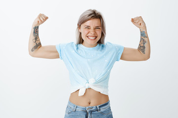 Show me real power of muscles. Portrait of good-looking playful and emotive girl with tattooed...