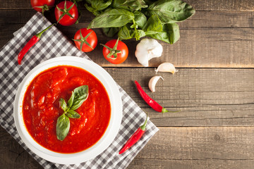 Fresh, healthy tomato soup with basil, pepper, garlic, tomatoes and bread on wooden background. Spanish gazpacho soup.