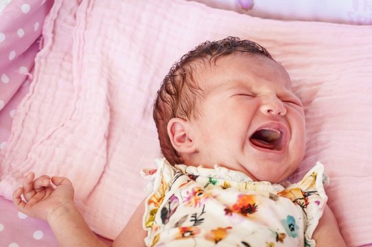 Hungry Caucasian newborn infant baby girl crying hard asking for mother's milk. Crying baby stock image. Open mouth.