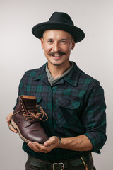 Positive moustached shoemaker with a handsome apperance wearing casual clothing, holding custom...
