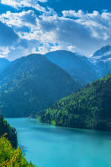 Beautiful Lake Ritsa in the Caucasus Mountains. Green mountain hills, blue sky with clouds. Spring landscape.