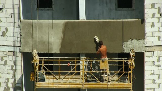 Building. Cranes, skyscrapers, high-rise buildings. City projects. The plaster works. He applies a solution of cement and speaks on his mobile phone.