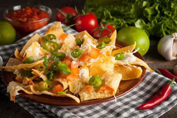 Mexican nachos with tortilla, hot pepper, melted cheese, ketchup and white sauce, jalapeno and lime on wooden background. Fast food and junk food concept. Chili con carne.