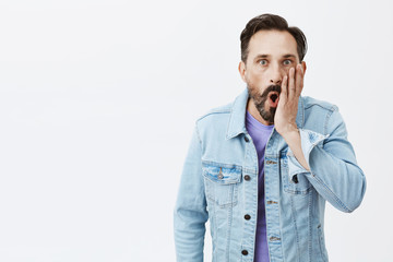 Man seeing car bumped in his bike, shocked and speechless. Portrait of stunned handsome mature male model with beard in denim jacket, dropping jaw and holding palm near mouth, being amazed