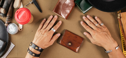 Leather goods master hands and handmade leather wallets lay on table with crafting tools. Workflow in the workshop. Workflow in the workshop, close-up.